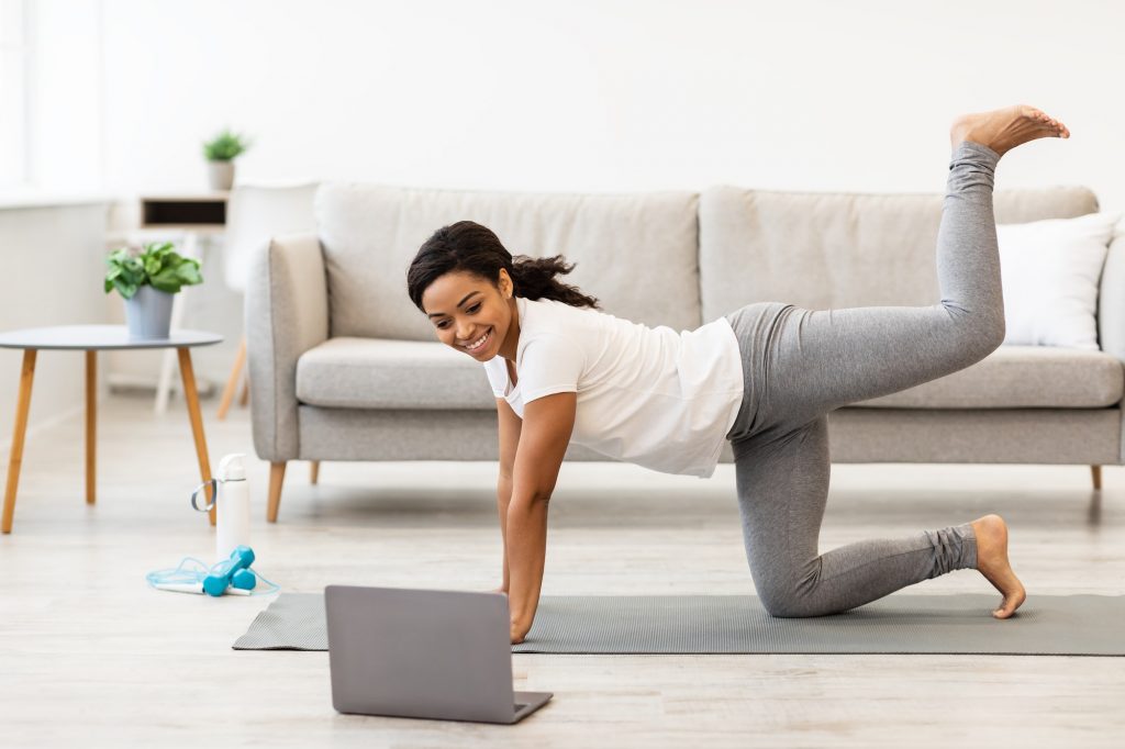 Black woman exercising at home watching tutorial on laptop