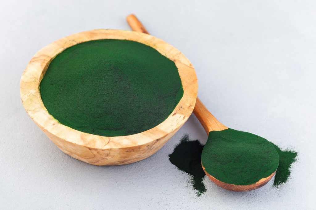 Superfood chlorella powder superfood in wooden bowl and spoon, horizontal, closeup